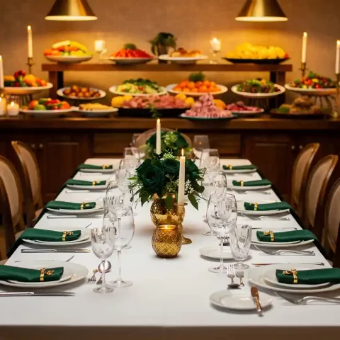 Elegante banquettafel met fijn porselein en gepolijst zilverwerk op wit linnen, verlicht door kaarsen en hanglampen in gouden sfeerverlichting.