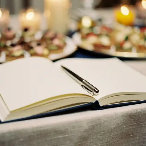 Open gastenboek met elegante pen op linnen gedekte feesttafel, zachte gouden kaarslichtsfeer op de achtergrond.