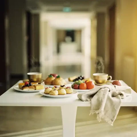 Elegante foyer pauzehoek met mini-gebakjes, vers fruit en dampende koffie op een wit statafel, zachte gouden verlichting op de achtergrond.